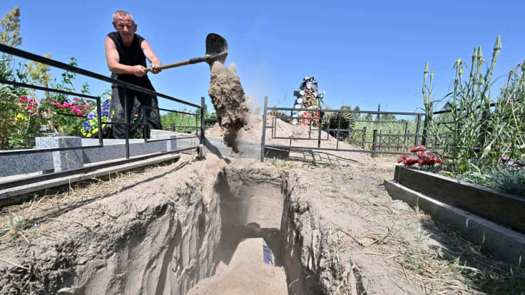 Työntekijä lapioi hiekkaa hautaan.