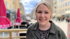 Tampereen kaupungin tapahtumatuottaja Matilda Salminen paljain päin. Kuvattuna kadulla, ja taustalla näkyy terrasien punaisia, suljettuja aurinkovarjoja. 