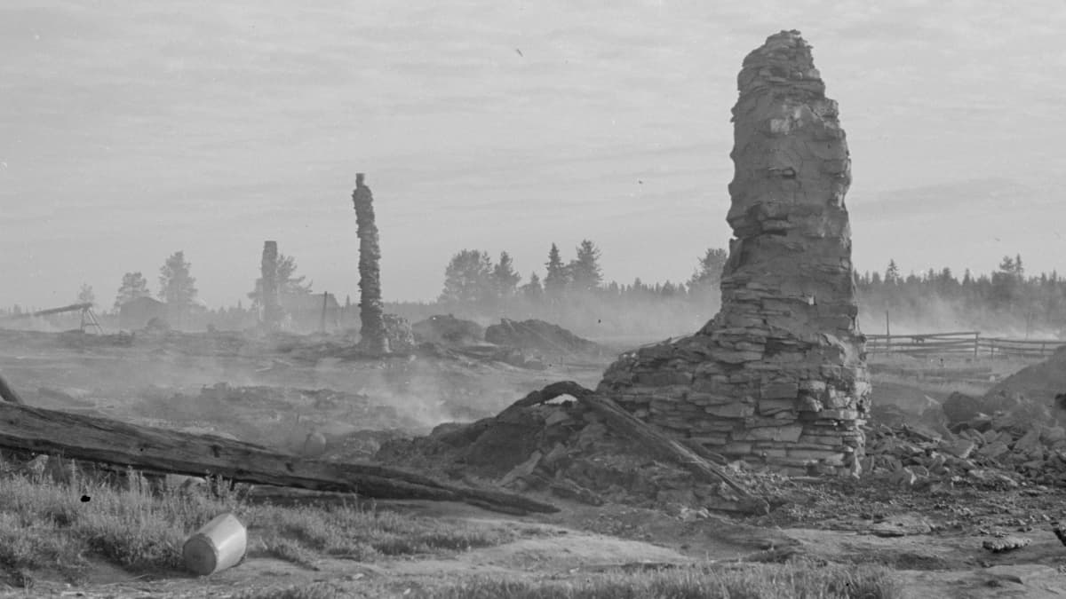 Mustavalkoinen kuva partisaanien tuhoamasta Lokan kylästä, savuavasta maasta törröttää savupiippujen raunioita.
