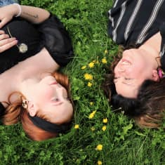 Päivi Sappinen ja tytär Vilma Sappinen makaavat ruohikolla toisiaan katsoen ja hymyillen.