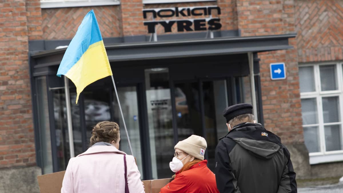 Mielenosoittajia Nokian Renkaiden konttorin edessä Ukrainan lipun kanssa.
