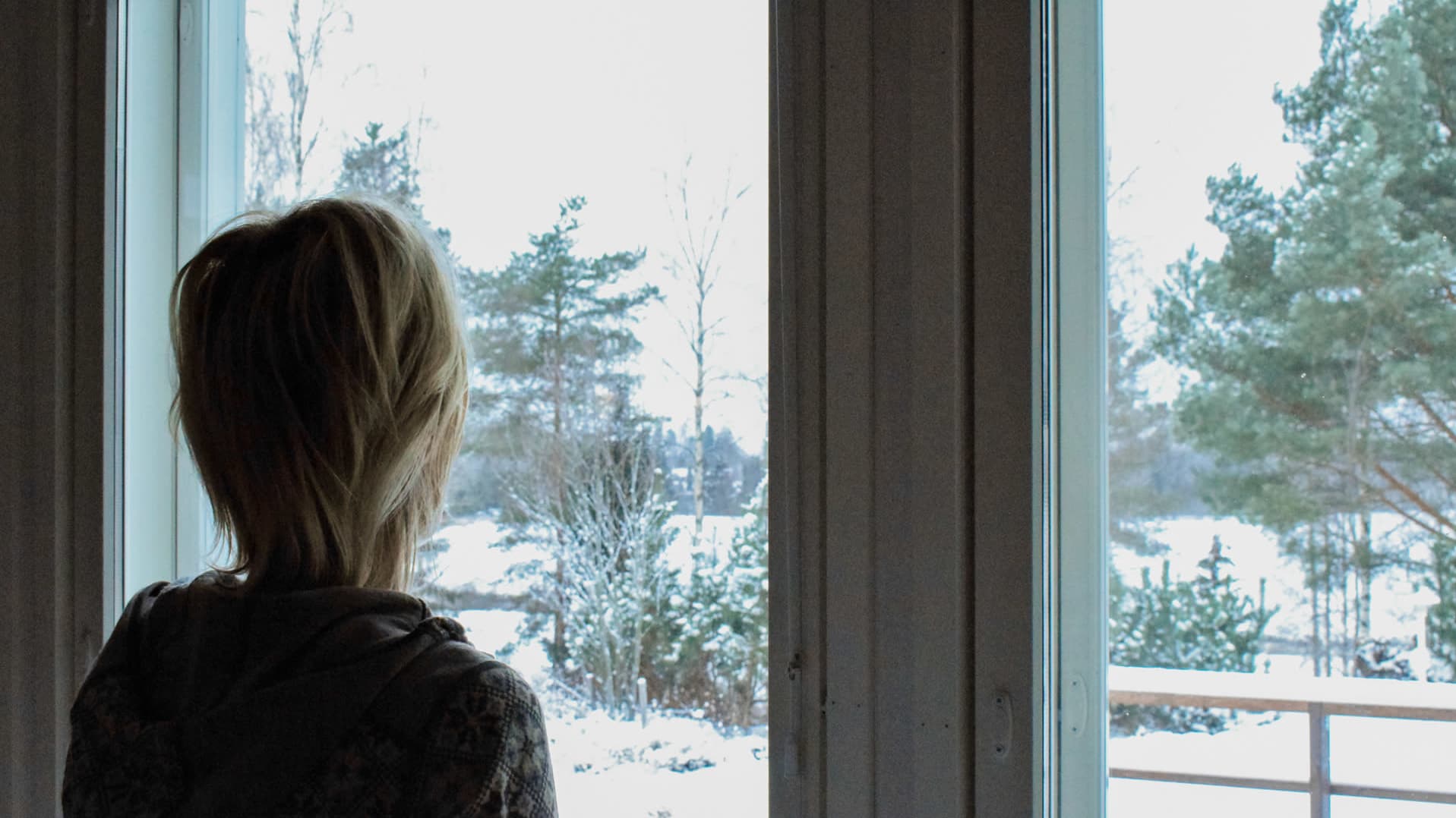 Anonyymina haastateltu henkilö katselemassa ikkunan edessä lumista talvimaisemaa. 