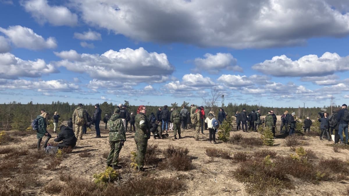 Poutapilvisellä peltoaukealla on on ihmisiä, joista osa on pukeutunut armeijan vaatteistiin.
