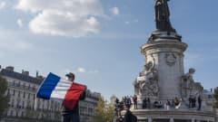 Mies pitelee Ranskan lippua aukiolle, jossa on myös paljon muita ihmisiä.