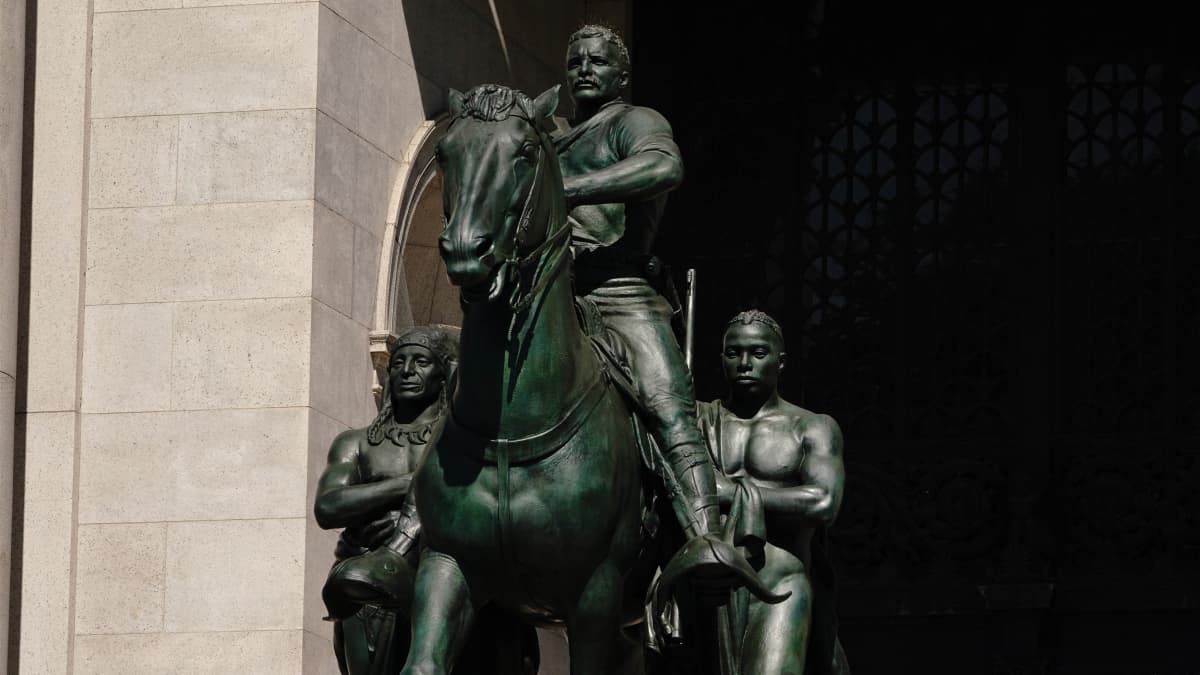 Patsas, jossa Theodore Roosevelt on ratsun selässä. Vierellä seisomassa afroamerikkalaista ja Pohjois-Amerikan alkuperäisasukasta esittävät hahmot.
