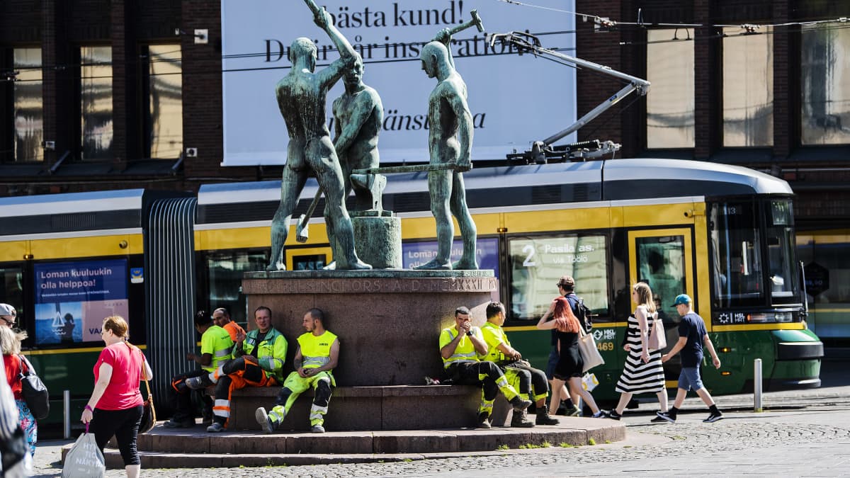 Kuvassa rakennusmiehet istuvat Kolmen sepän patsaalla heinäkuussa 2020.