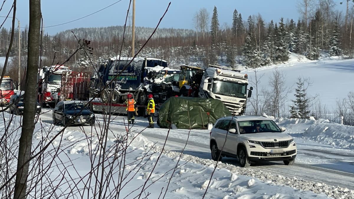 Rekka tien reunassa, kyydissään jätteenkuljetusauto. Rekan edessä pressu. Ohiajavaa henkilöautoliikennettä, pelastushenkilökuntaa tien reunassa. 