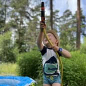 Kolmevuotias Urho Tuominen suihkuttaa vettä letkulla kahluualtaan vieressä.