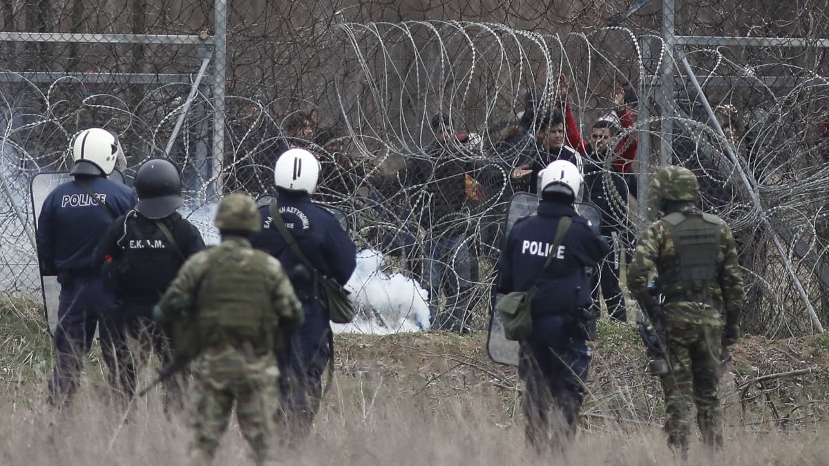 Kreikkalaisia poliiseja piikkilanka-aidan edessä, toisella puolella Turkista pyrkiviä siirtolaisia.