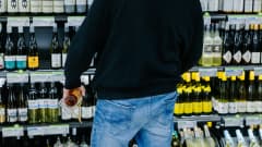 Mies seisoo viinihyllyjen edessä kädessään jallupullo.