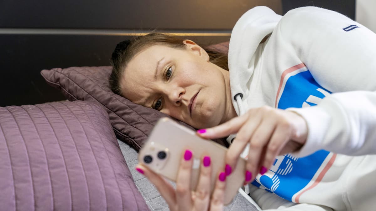 Jaana Saukko makaa sängyllä ja selaa puhelinta.