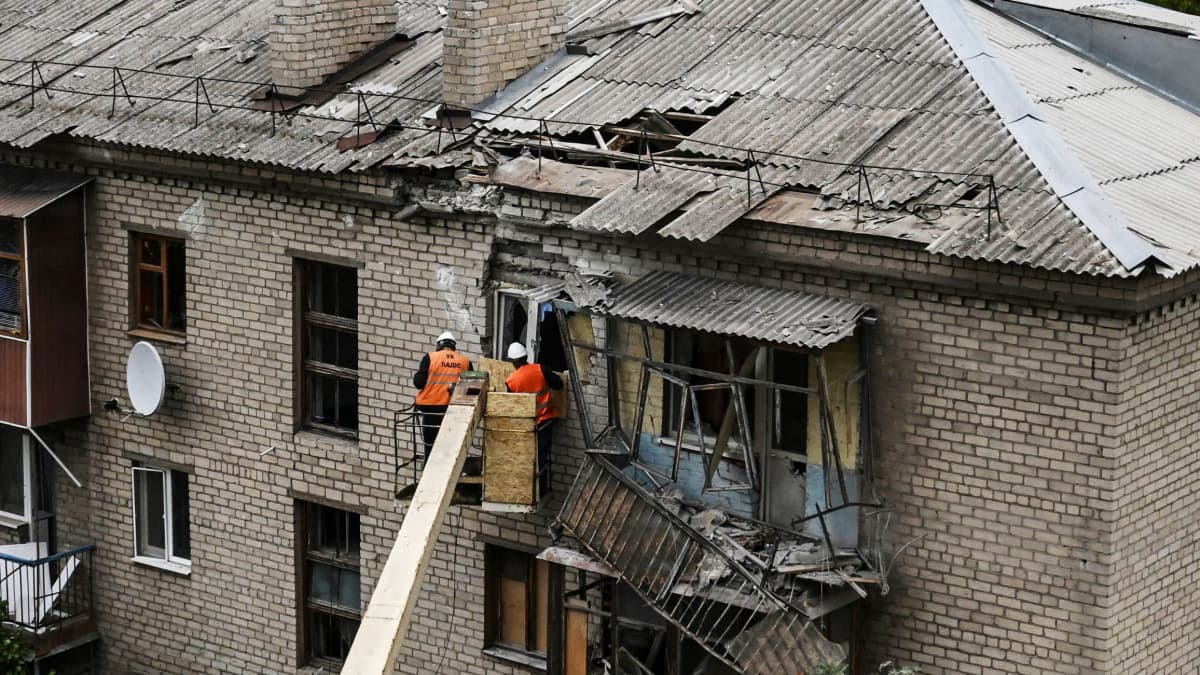Työntekijät korjaavat asuintalon osittain tuhoutunutta julkisivua.