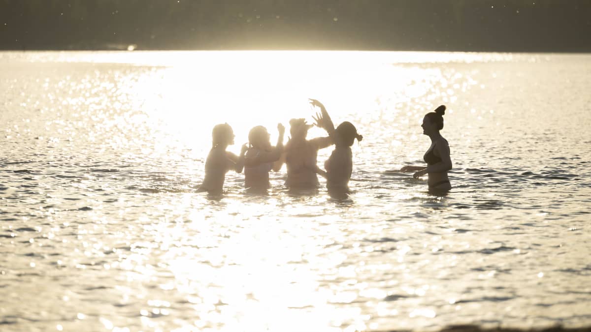 Nuoria naisia uimassa. Aurinko loistaa veteen.