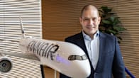 A smiling, short-haired man in a blazer and open-necked shirt stands by a model of a white Finnair plane.