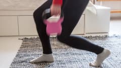 Nainen treenaa kahvakuulalla olohuoneen lattialla.
