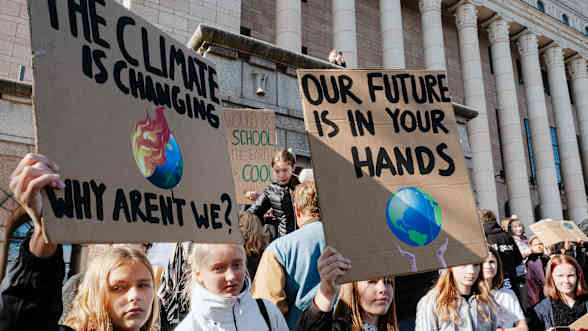 A row of girls or young women in front of Parliament, holding cardboard signs with hand-written climate slogans in English. 