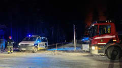 Poliisiauto, paloauto ja pelastushenkilöstöä pimeässä tienristeyksessä. Taustalla tulipalon loimotus.