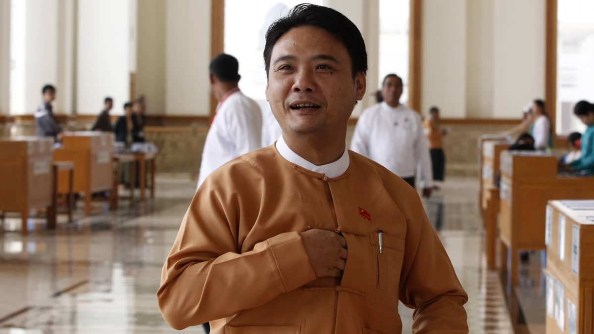Mies, Phyo Zeya Thaw, seisoo Myanmarin parlamentin salissa, päällään perinteinen takki, käsi napituksen aukossa. 