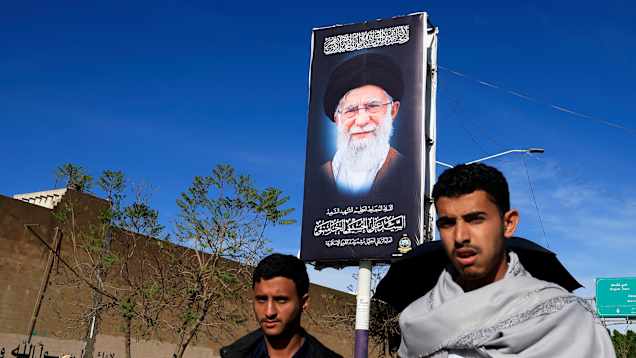 Kaksui henkilöä kävelee Ali Khamenein muistomainostaulun vieressä.