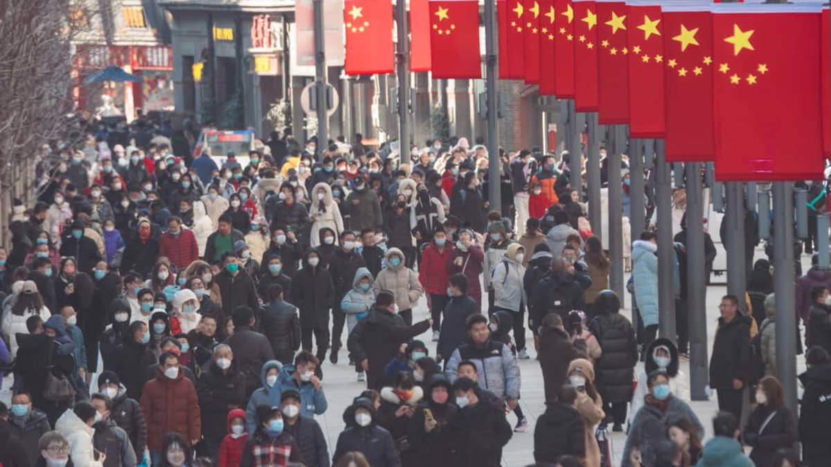 Paljon ihmisiä kadulla, suurimmalla osalla kasvomaski. Keskellä katua on tankorivistö, jossa riippuu Kiinan lippuja. 
