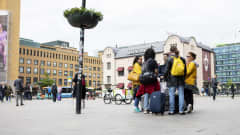 Ihmisiä seisoo pienessä ringissä matkalaukkujen ja reppujen kanssa Elielinaukiolla.