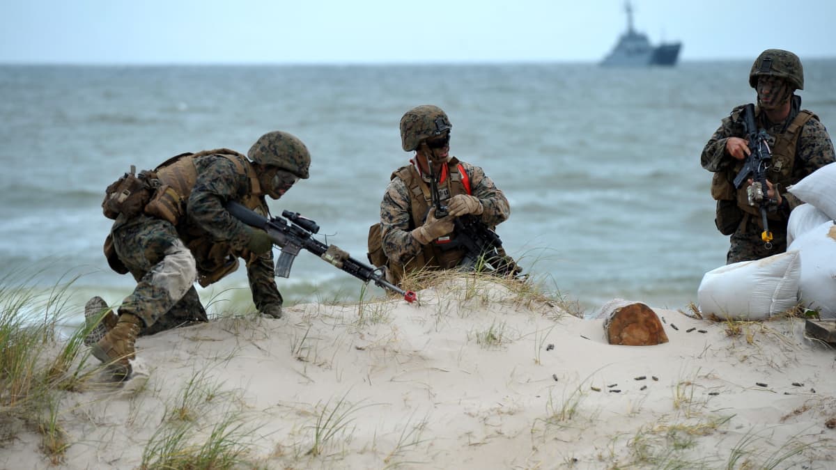 Sotilaita hiekkatöyräällä meren rannalla ja laiva takana merellä.