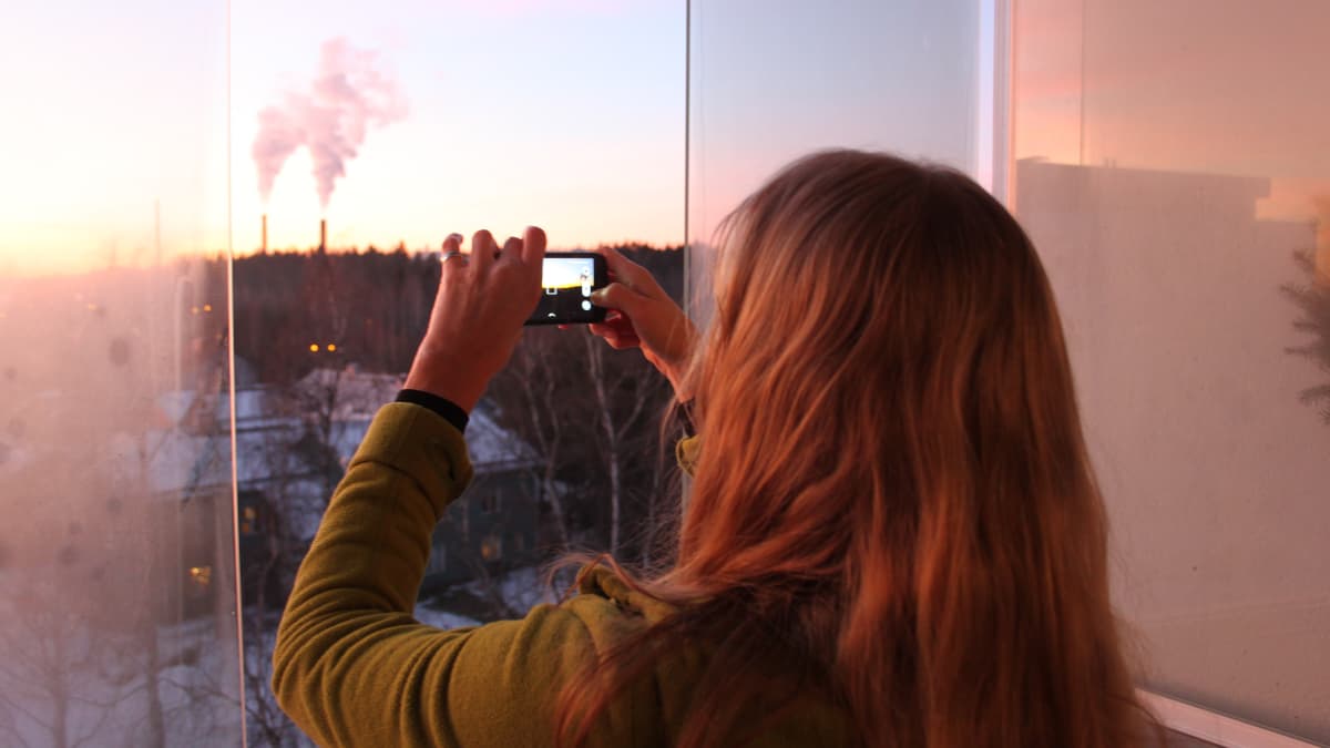 Nainen kuvaa parvekkeelta auringonlaskua kännykkäkameralla.