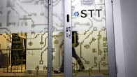 Glass door with the logo of Finnish News Agency "STT" on it. A person walking to the left can be seen through the glass.