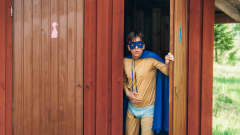 Supersankariasuun pukeutunut mies tulee ulos ulkokäymälästä vatsaansa pidellen.