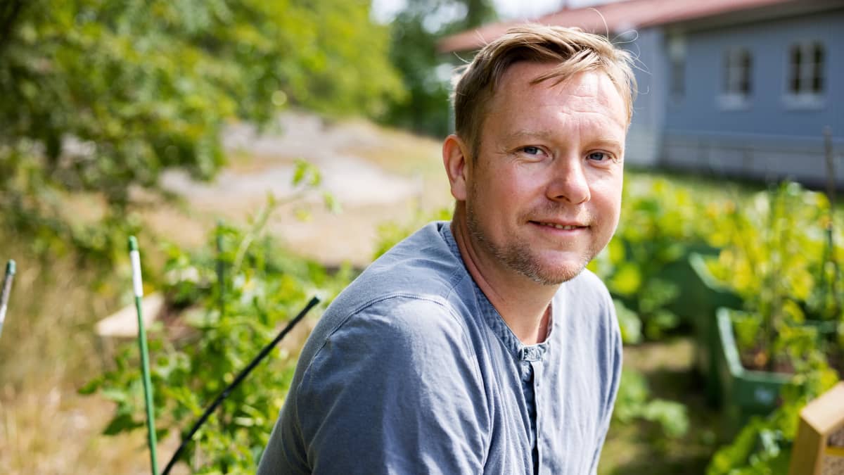 Mies katsoo kameraan ulkona taustallaan kasvillisuutta.