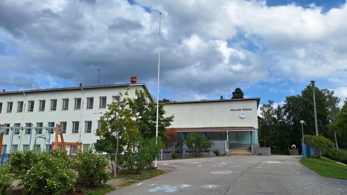 Vaaleankeltaisen koulurakennuksen seinässä lukee teksti Kuljun koulu. Rakennuksen edessä on valkoinen lipputanko.