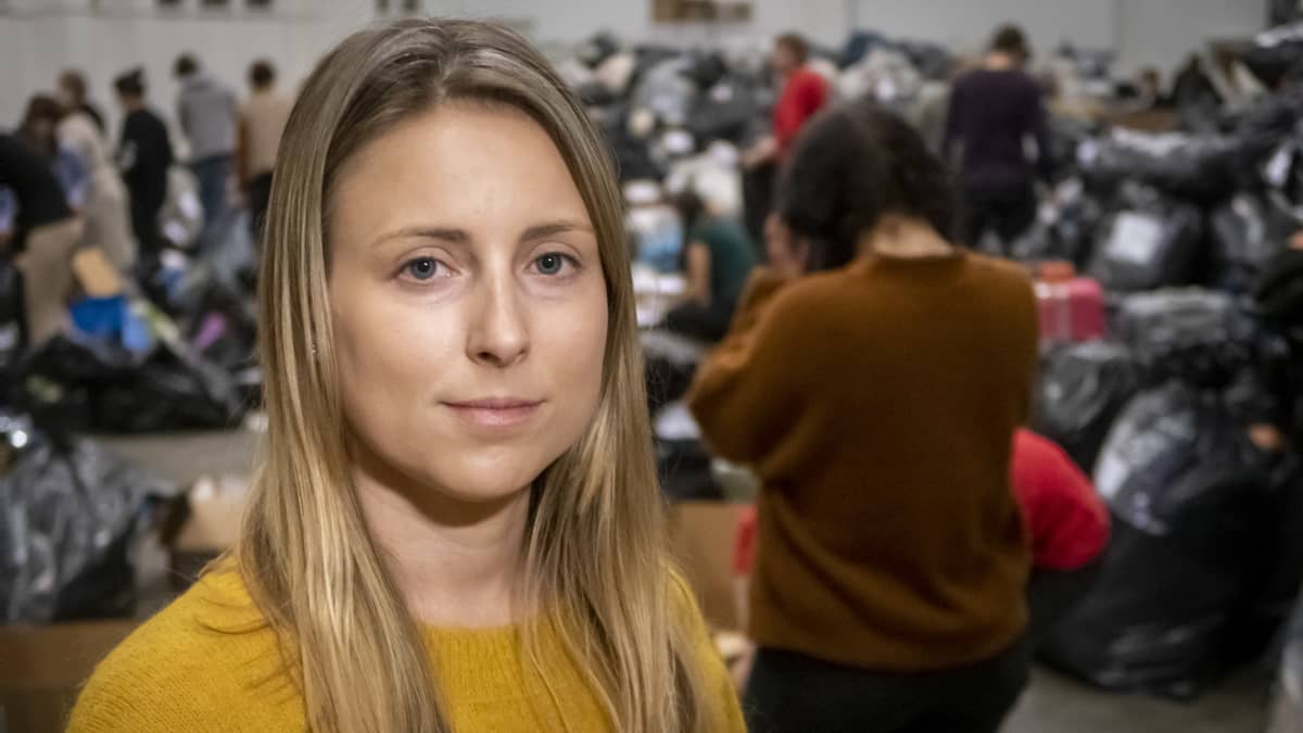 Keltapaitainen nainen hallissa, jossa paöljon tavaraa ja ihmisiä.