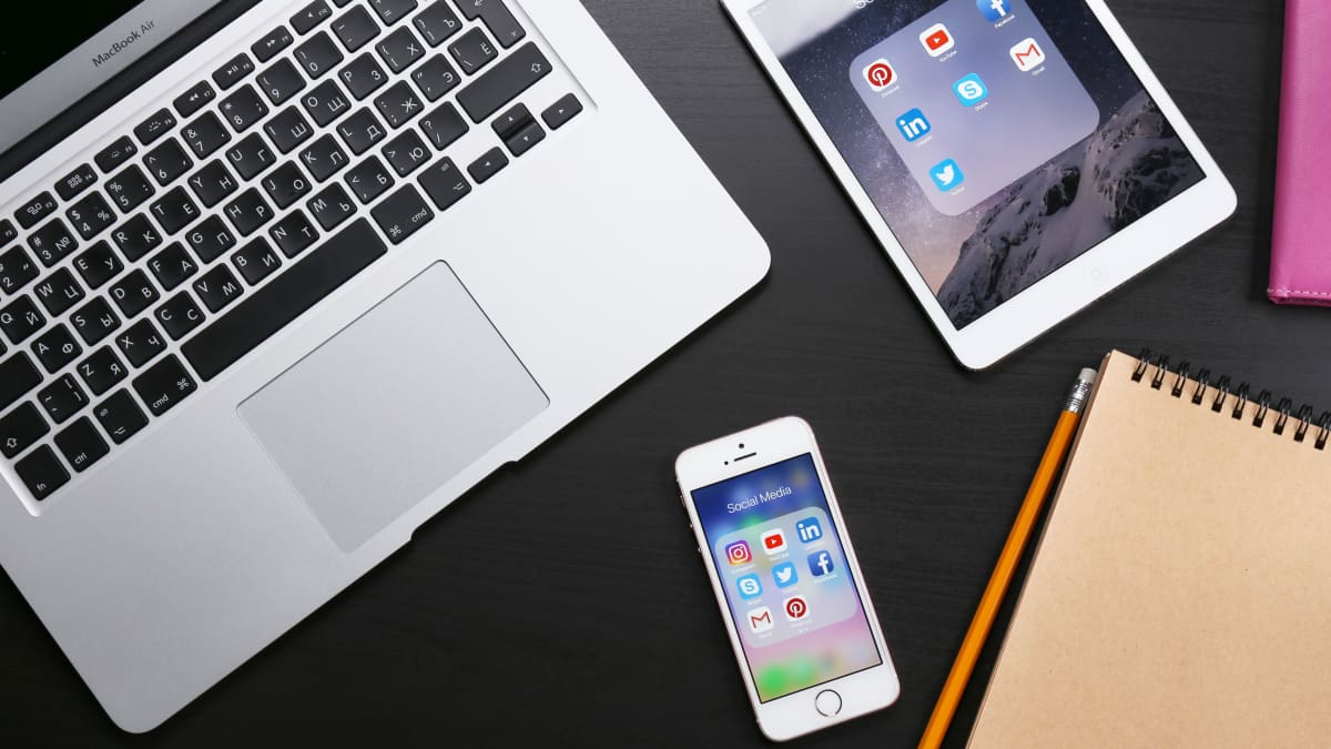 En iPhone, iPad och Macbook på ett bord.