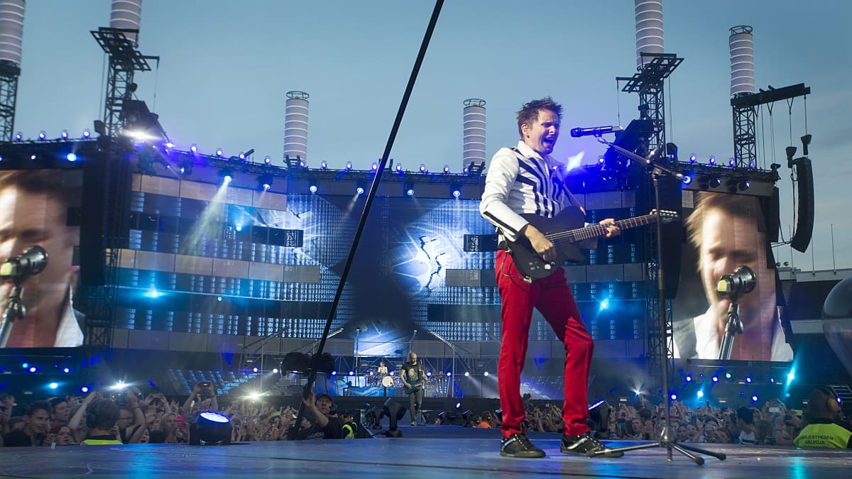 Rockyhtye Muse lavalla. Kitaristi, isot videoscreenit taustalla.