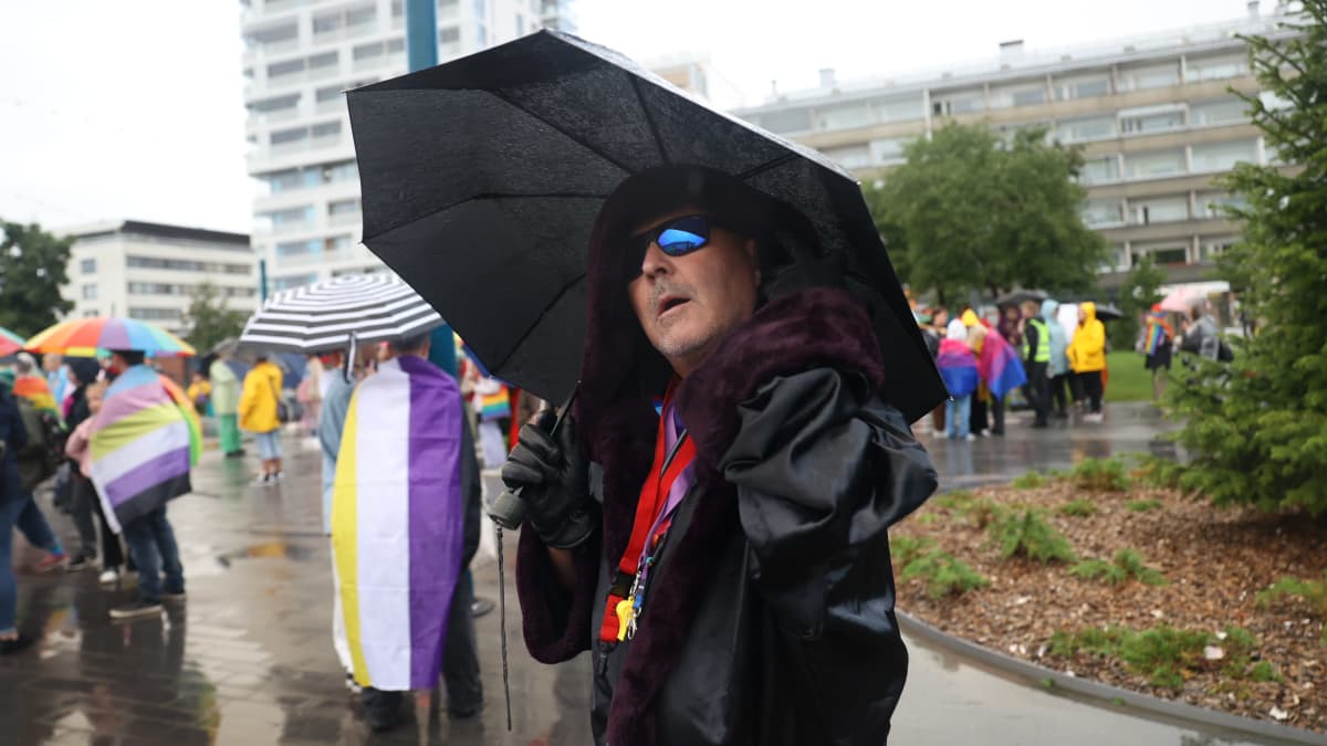 Tummiin pukeutunut henkilö pitää mustaa sateenvarjoa käsissään ja poseeraa kameralle