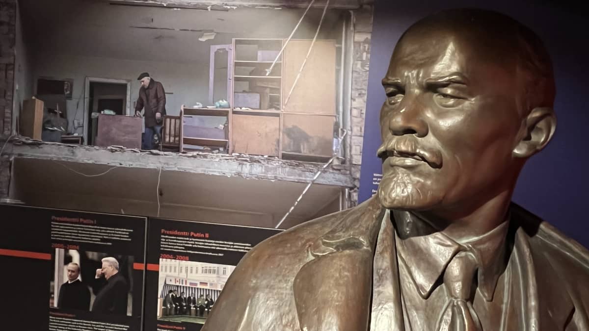 Etualalla on Leninin patsas, sen takana näkyy uutiskuvia Ukrainan sodan tuhosta.