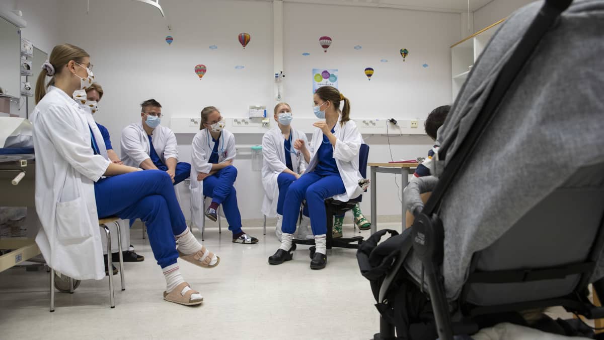 Lääketieteen opiskelijat istuvat ja kuuntelevat lastenkirurgi Susanna Porela-Tiihosen opetusta sairaalan vastaanottohuoneessa.