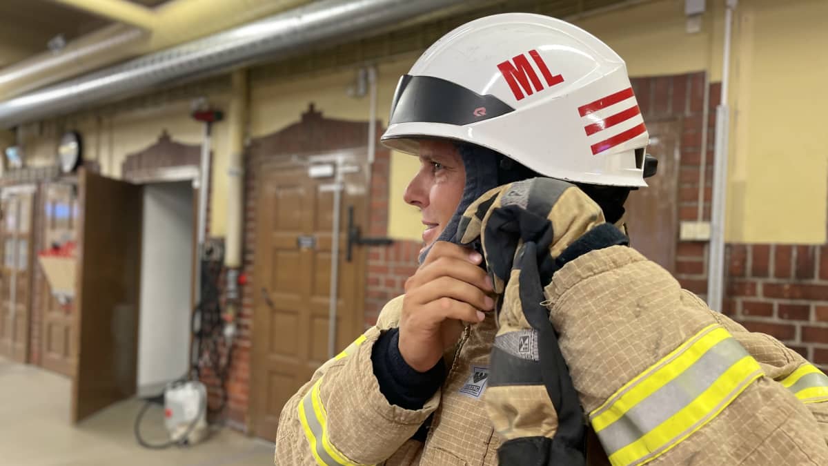 Palopelastaja pukee ylleen suojavarusteita, viimeiseksi kypärä