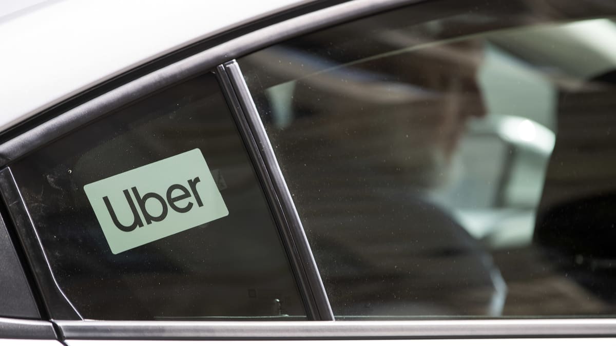 Uber-kuljettaja istuu autossa. Auton ikkunassa on Uber-tarra.