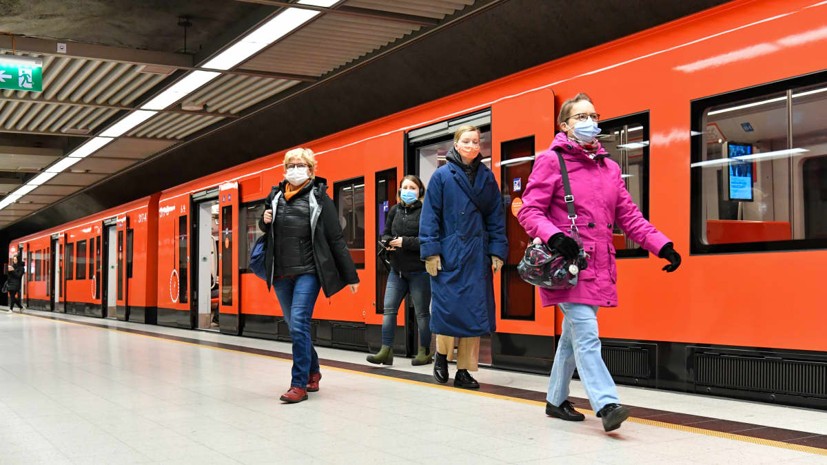 Människor i munskydd går ut ur en metro i Helsingfors.