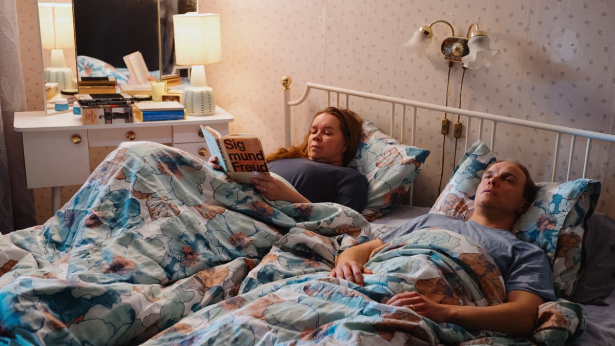 Pariskunta sängyssä. Nainen lukee kirjaa.