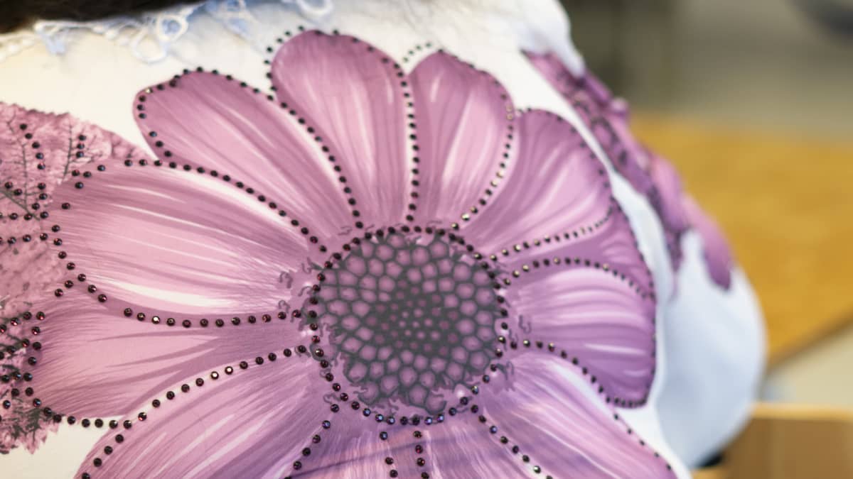 Kansallispuvun paidan selkäpuolella on helmin koristeltu violetti kukka.
