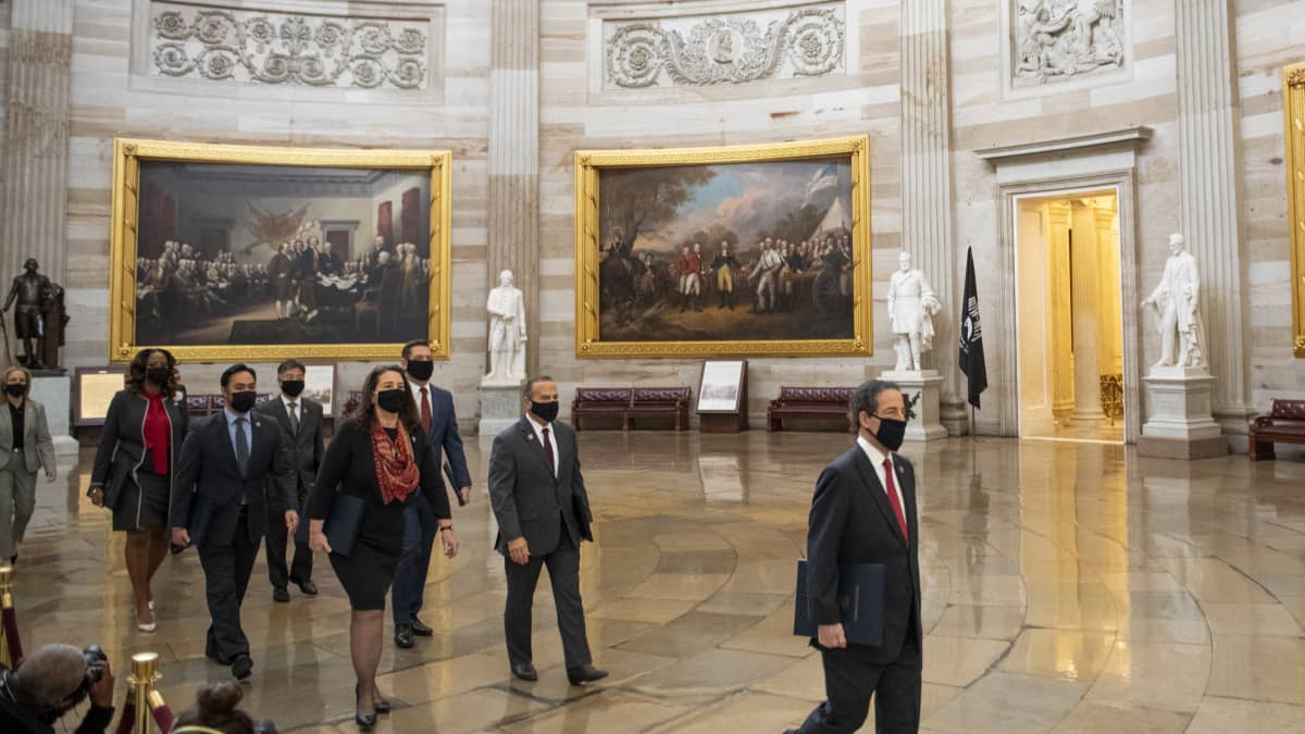 Kongressiedustajat kävelevät koristeellisen salin halki maskit kasvoillaan