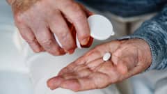 Åldrade händer häller ut en tablett från en medicinburk i handflatan.
