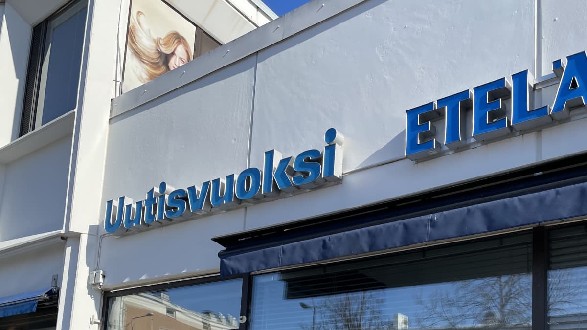 Marki Markkanen Uutisvuoksi-lehden toimituksen ulko-oven vieressä. Aurinko paistaa.