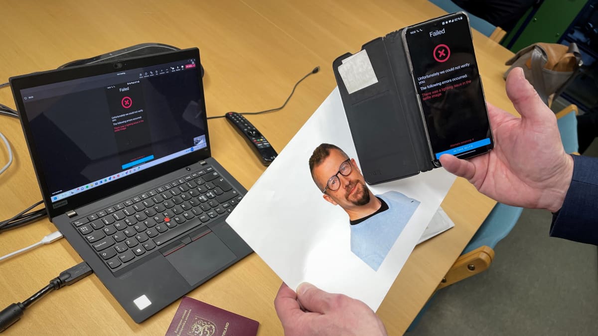 Kannettava tietokone pöydällä ja sen vieressä Suomen passi. Etualalla valokuva miehestä ja kännykästä kuvan päällä.
