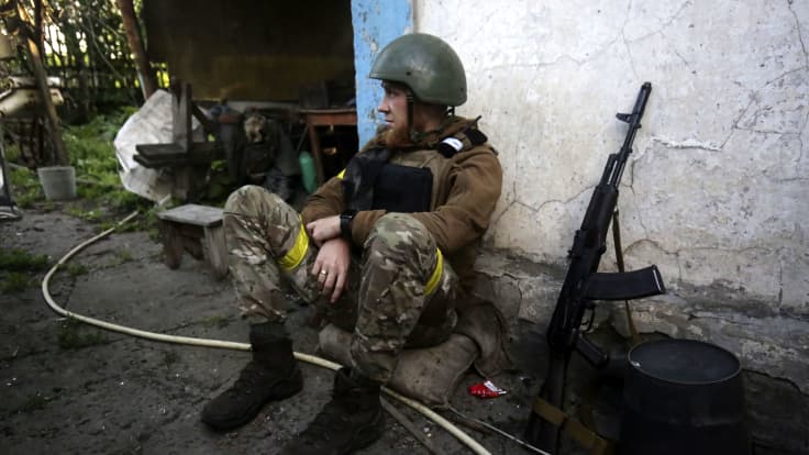 Sotilas istuu maassa ase vieressään.