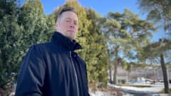 Turun reserviläiset ry:n Joose Olli musta takki yllään katsoo kohti kameraa, taustalla näkyy pensaita ja puita.