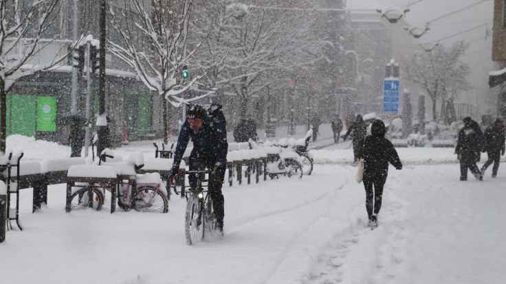 Ihmisiä kävelemässä ja pyöräilemässä Turussa Kauppatorilla. Lunta sataa voimakkaasti ja maassa on runsaasti lunta.