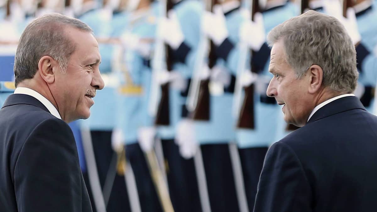 Recep Tayyip Erdogan ja Sauli Niinisto katsovat toisiinsa. Taustalla uniformupukuisia ihmisiä rivissä aseet kädessään.